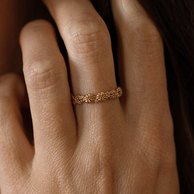 Close up of a hand with a gold floral-etched ring band with textured marigold flowers and small clear gemstones.