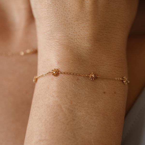 A lifestyle image of a dainty gold bracelet on a person's wrist with stationary textured chrysanthemum flowers with small accent stones in the center along the chain.