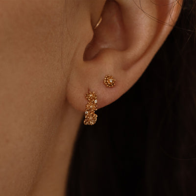 Close-up of a person wearing gold hoop earrings made up of a textured floral design and a matching stud earring with a singular floral motif.