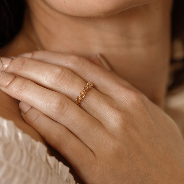 Close up of a hand with a gold floral-etched ring band with textured chrysanthemum flowers and small clear gemstones.