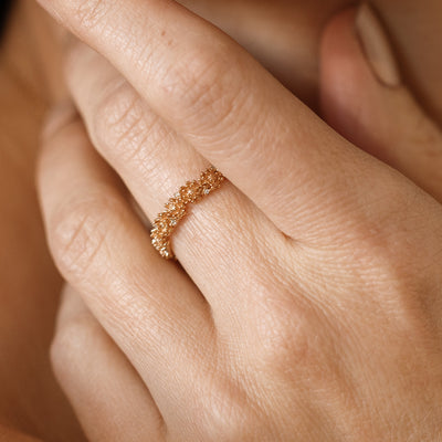 Close up of a hand with a gold floral-etched ring band with textured chrysanthemum flowers and small clear gemstones.