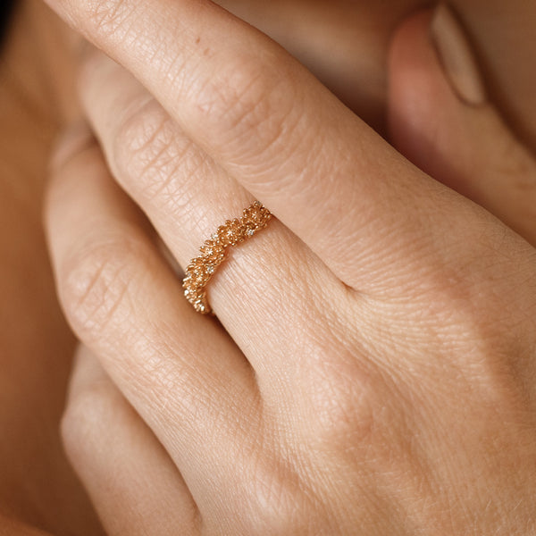 Close up of a hand with a gold floral-etched ring band with textured chrysanthemum flowers and small clear gemstones.