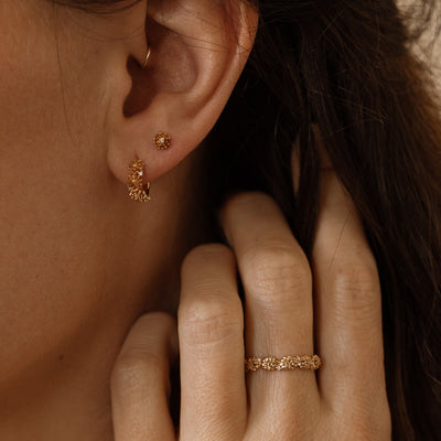 Close-up of a person wearing gold hoop earrings made up of a textured floral design and a matching stud earring with a singular floral motif.