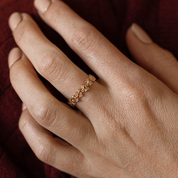 Close up of a hand with a gold floral-etched ring band with textured holly flowers and small clear gemstones.