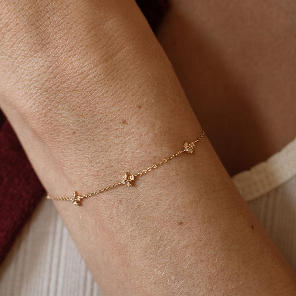 A lifestyle image of a dainty gold bracelet on a person's wrist with stationary textured holly flowers with small accent stones in the center along the chain.