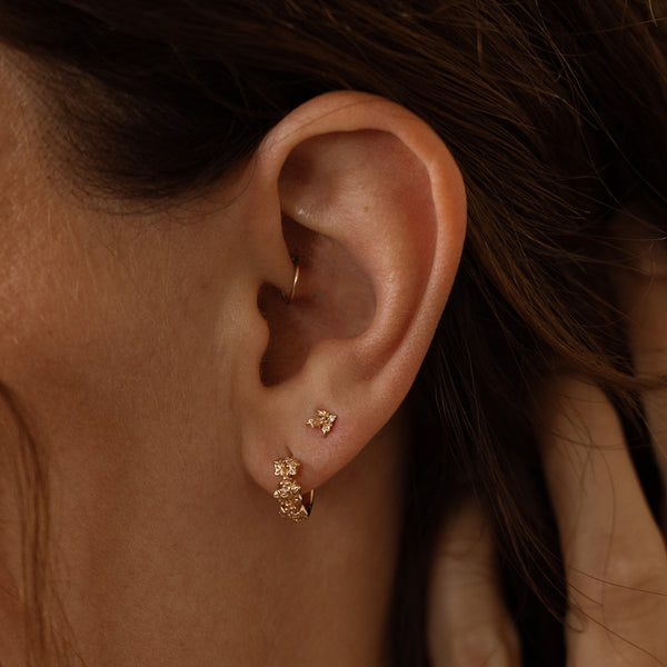 Close-up of a person wearing gold hoop earrings made up of a textured floral design and a matching stud earring with a singular floral motif.