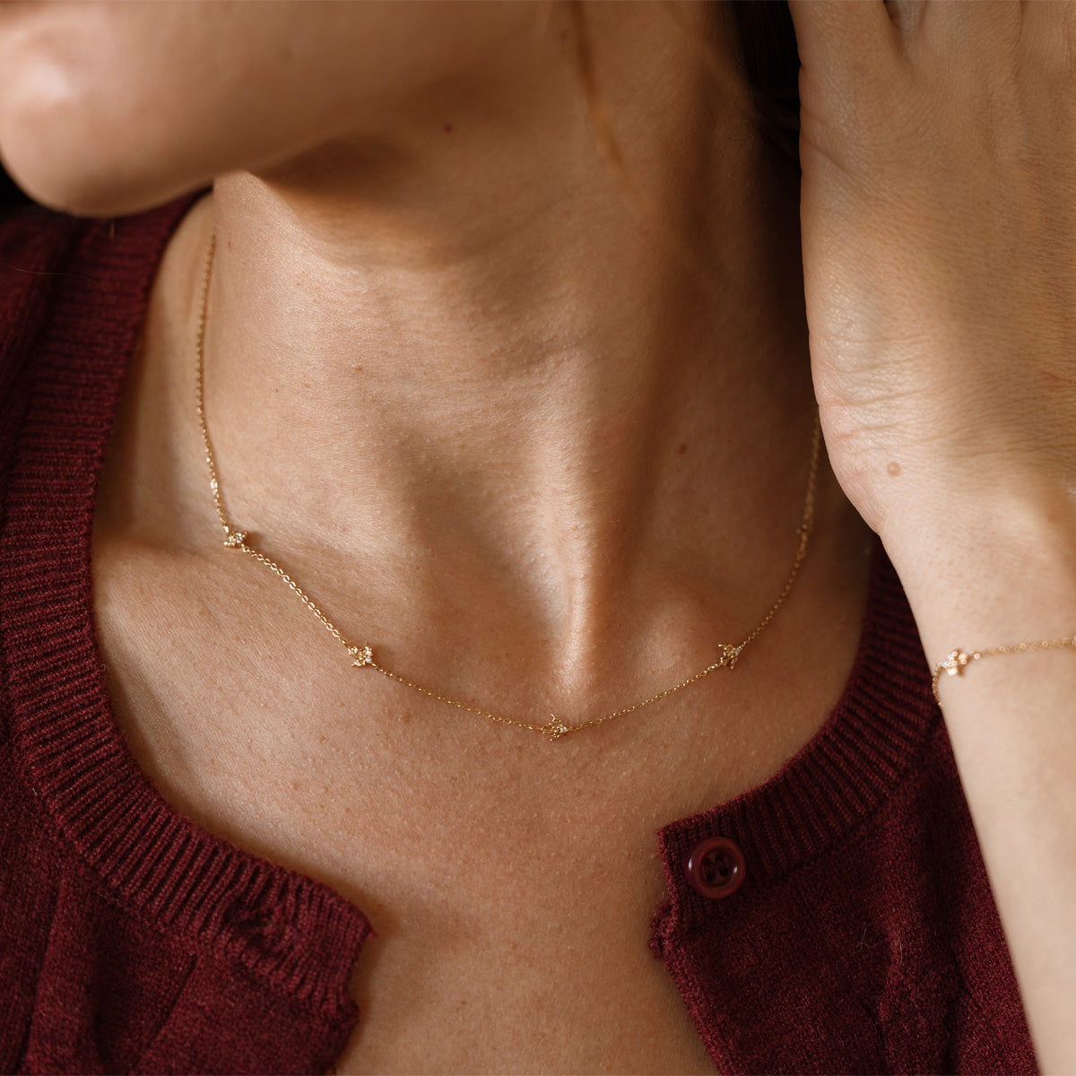 A lifestyle image of a dainty gold necklace on a person's neck with stationary textured holly flowers with small accent stones in the center along the chain.