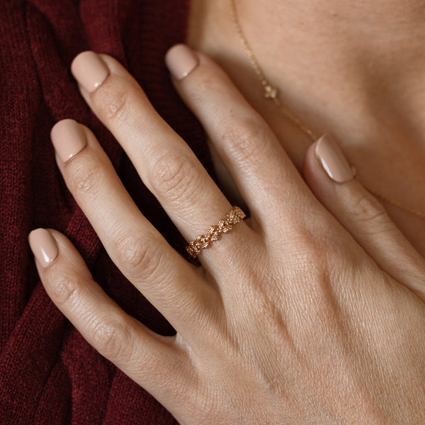 Close up of a hand with a gold floral-etched ring band with textured holly flowers and small clear gemstones.