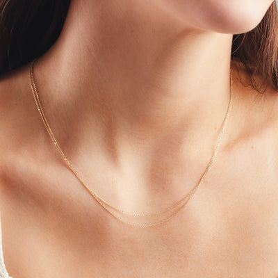 A close up shot of a person's neck wearing two gold delicate chains layered.