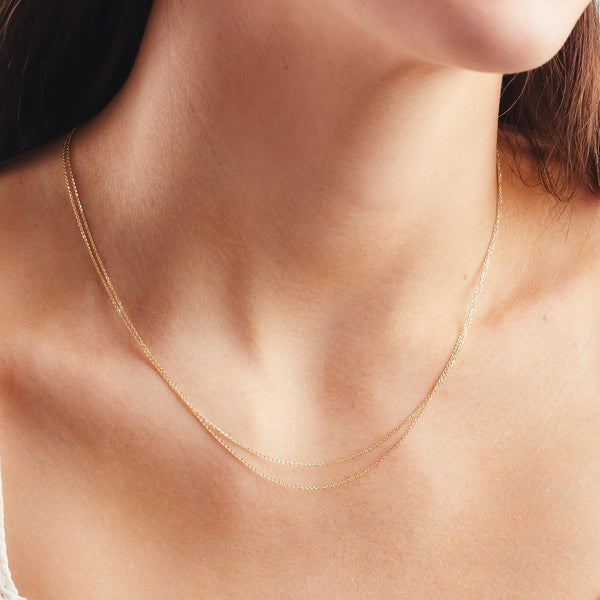 A close up shot of a person's neck wearing two gold delicate chains layered.