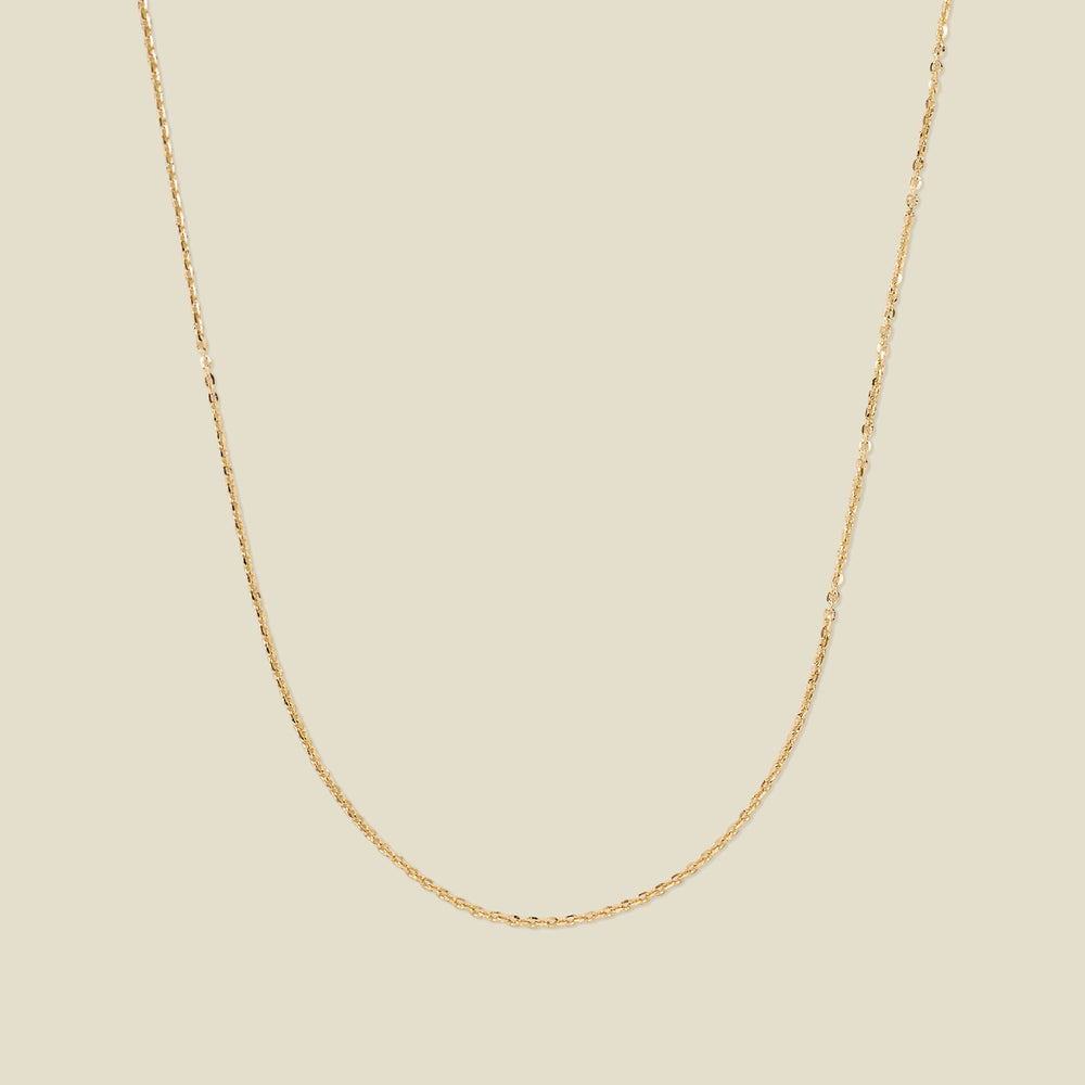 A dainty gold chain necklace draped in a U-Shape, set against a solid beige background.