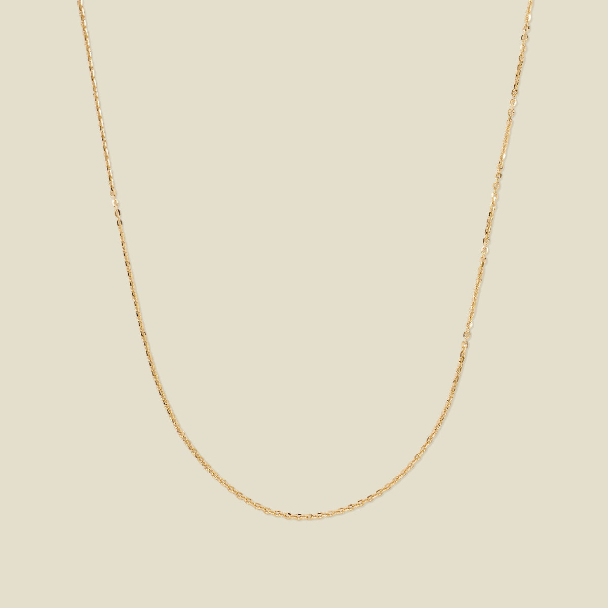 A dainty gold chain necklace draped in a U-Shape, set against a solid beige background.
