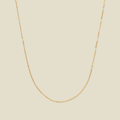 A dainty gold chain necklace draped in a U-Shape, set against a solid beige background.