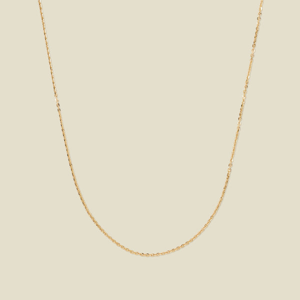 A dainty gold chain necklace draped in a U-Shape, set against a solid beige background.