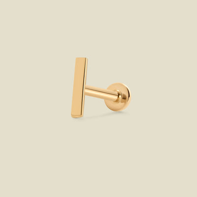 A single gold bar stud earring shown from a side profile view against a solid, warm off-white background.