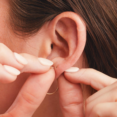 A lifestyle close up photo of a person putting in a flat back stud earring, with the back in the earring hole.