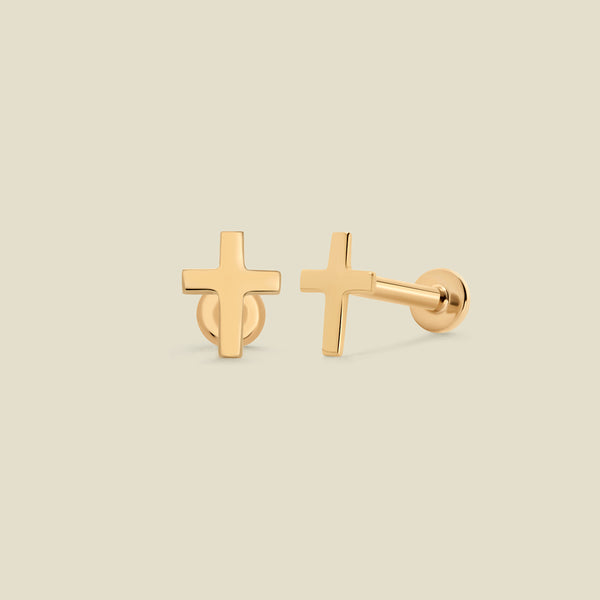 A pair of yellow-gold cross shaped stud earrings, with a flat backing, set against a solid beige background.