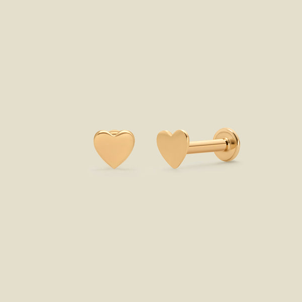 A pair of yellow-gold heart shaped stud earrings with a flat back, set against a solid beige background.