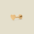 A single gold heart-shaped stud earring with a flat, polished finish, shown on a solid light beige background.