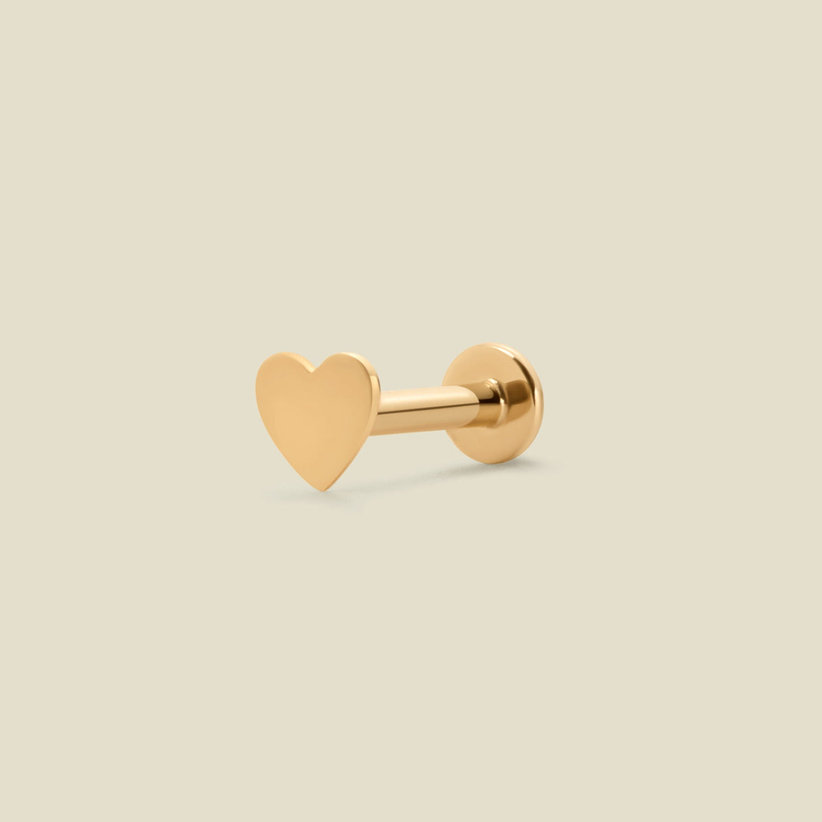A single gold heart-shaped stud earring with a flat, polished finish, shown on a solid light beige background.