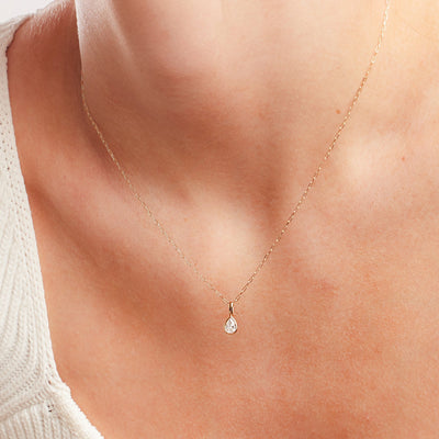 A close up shot of a person's neck wearing a delicate paperclip link gold chain with a singular pear-shaped bezel-set clear stone charm.