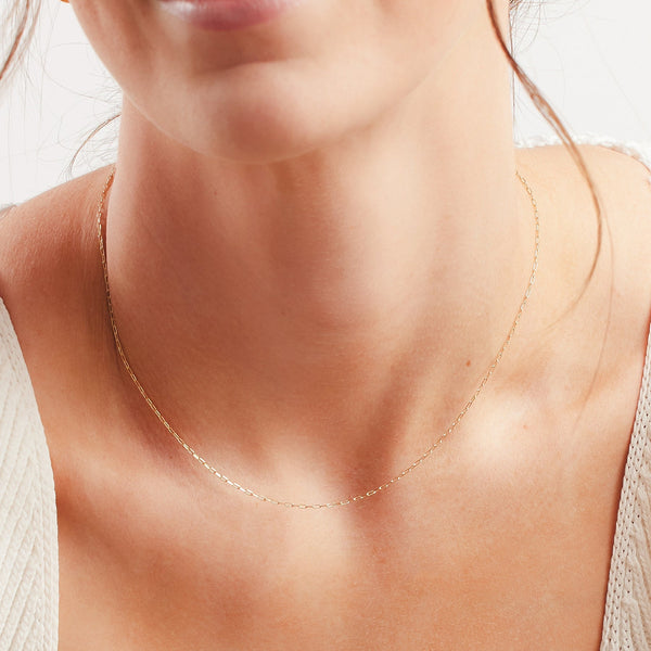 A close up image of a person's neck wearing a delicate paperclip link gold chain.
