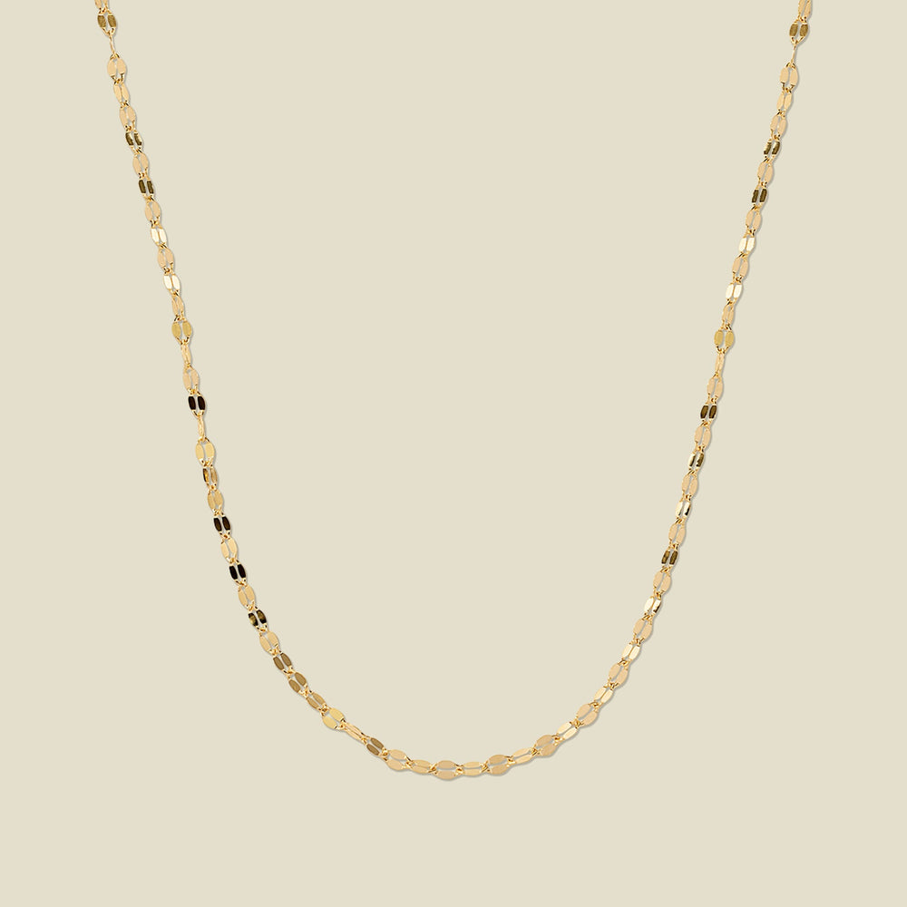 A textured, delicate gold chain necklace draped in a U-Shape, set against a solid beige background.