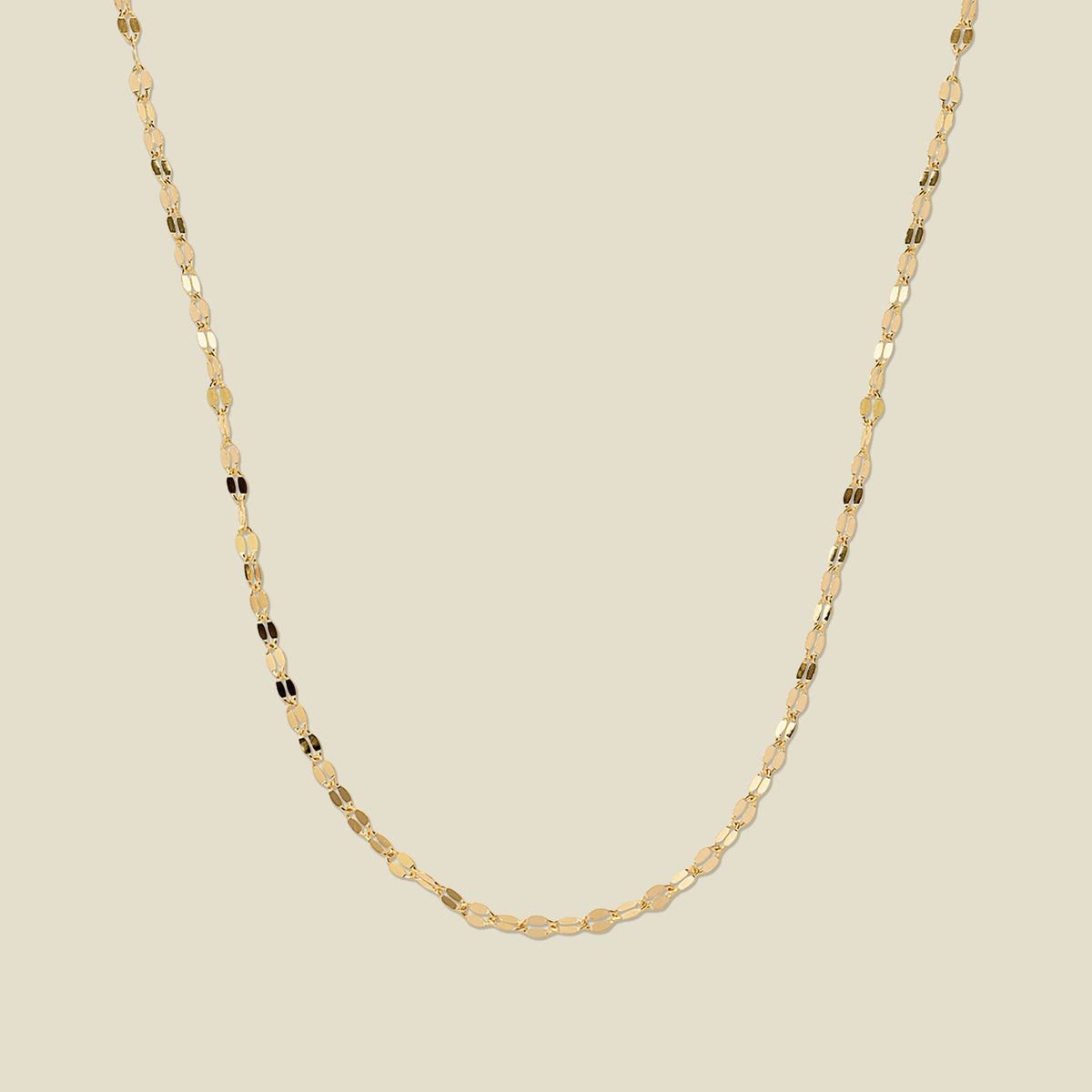 A textured, delicate gold chain necklace draped in a U-Shape, set against a solid beige background.