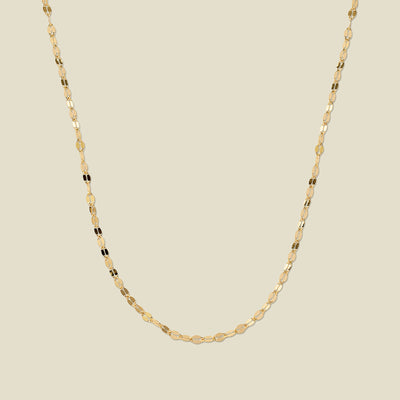 A textured, delicate gold chain necklace draped in a U-Shape, set against a solid beige background.