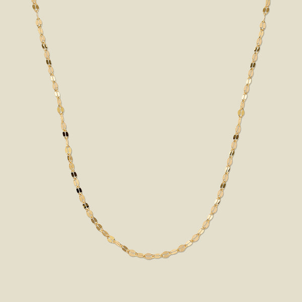 A textured, delicate gold chain necklace draped in a U-Shape, set against a solid beige background.