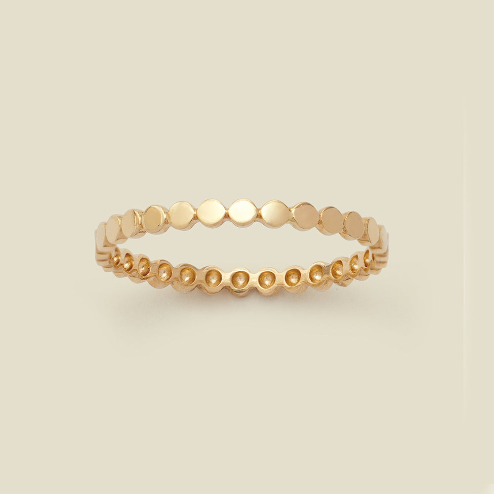 A yellow-gold eternity style ring with flattened circles set side-by-side around the band, set against a solid beige background.