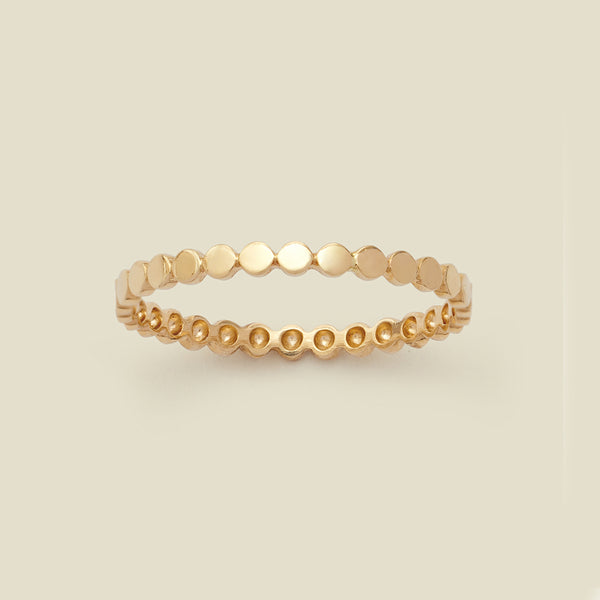 A yellow-gold eternity style ring with flattened circles set side-by-side around the band, set against a solid beige background.