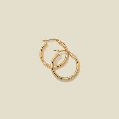 A pair of gold polished hoop earrings, stacked on one another, set against a solid beige background.
