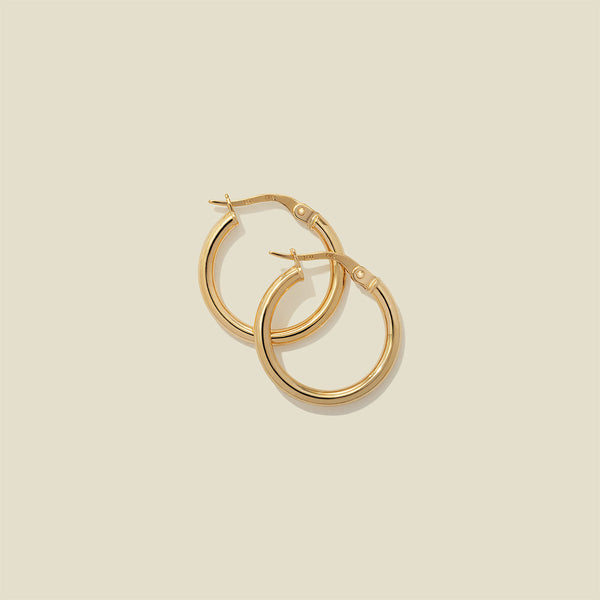 A pair of gold polished hoop earrings, stacked on one another, set against a solid beige background.
