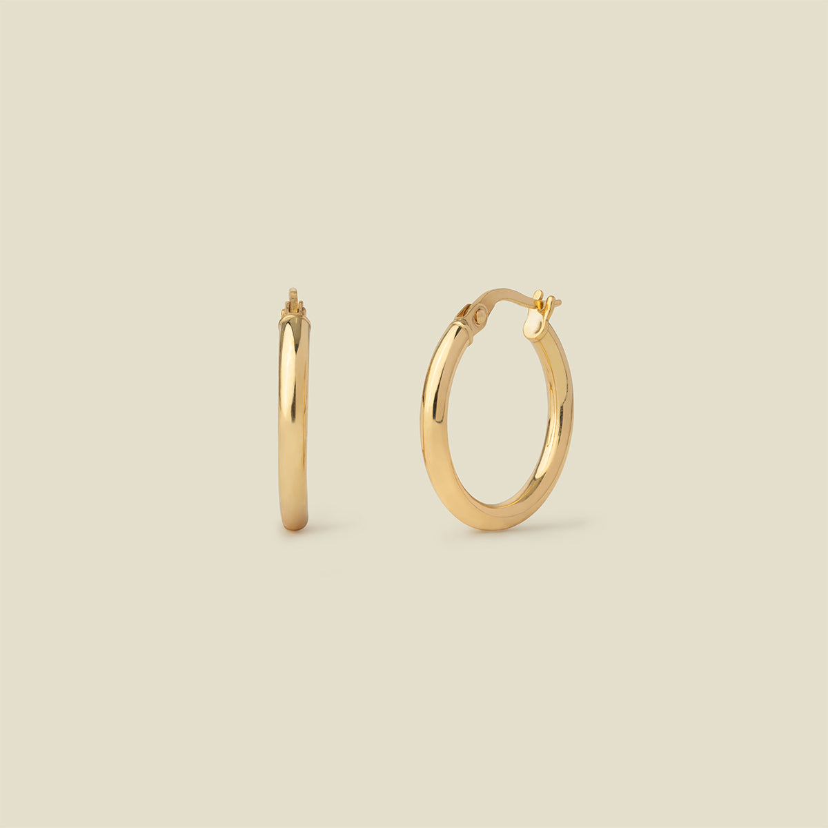 A pair of polished gold hoop earrings shown on a plain warm beige background, with one earring facing forward and the other in side view.
