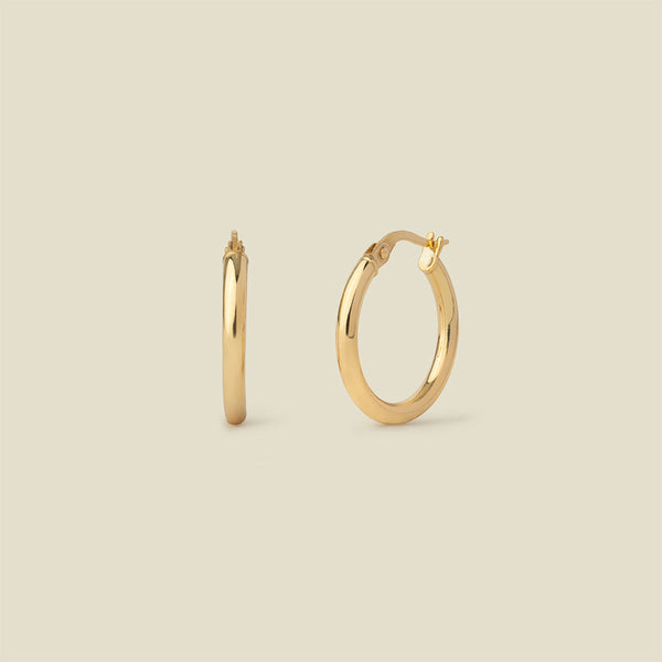 A pair of polished gold hoop earrings shown on a plain warm beige background, with one earring facing forward and the other in side view.