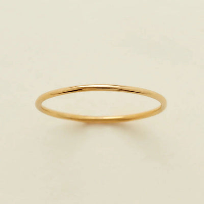 A minimalist, thin yellow gold band ring with a polished finish, displayed on a clean, solid off-white background.