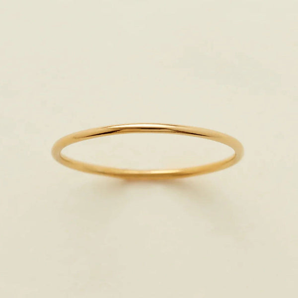A minimalist, thin yellow gold band ring with a polished finish, displayed on a clean, solid off-white background.