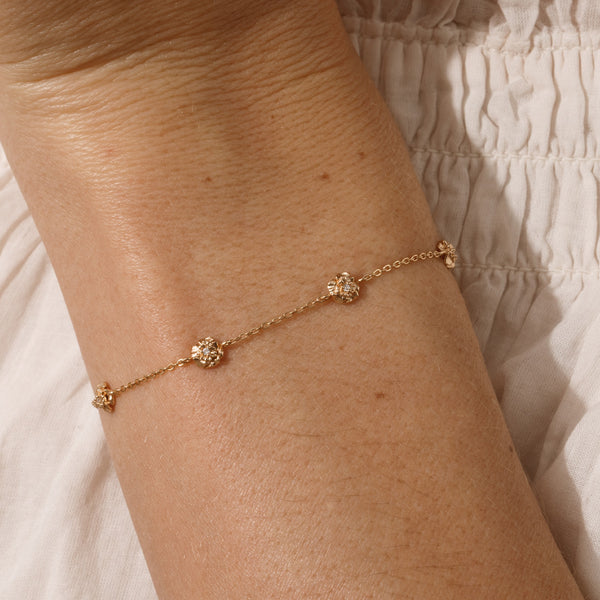 A lifestyle image of a dainty gold bracelet on a person's wrist with stationary textured carnation flowers with small accent stones in the center along the chain.