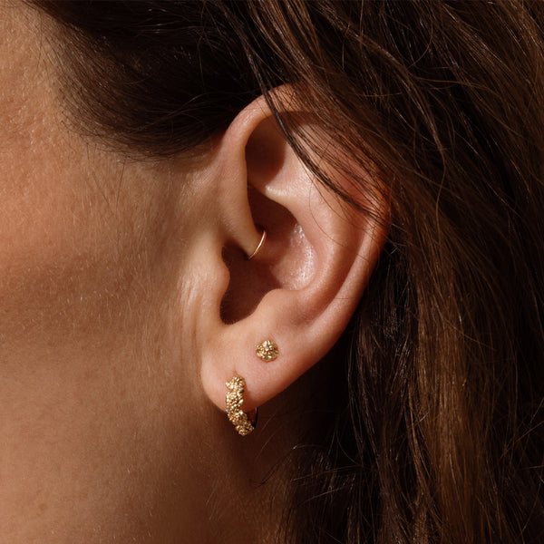 Close-up of a person wearing gold hoop earrings made up of a textured floral design and a matching stud earring.