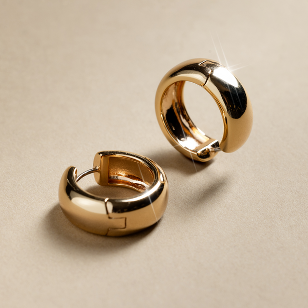 Two wide polished gold hoop earrings on a beige background