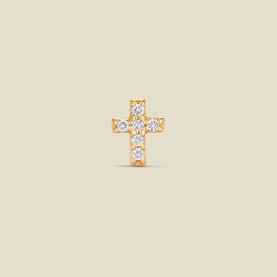 Gold cross earring with diamonds on a beige background
