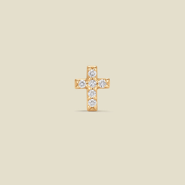Gold cross earring with diamonds on a beige background