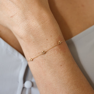 A lifestyle image of a dainty gold bracelet on a person's wrist with stationary textured violet flowers with small accent stones in the center along the chain.