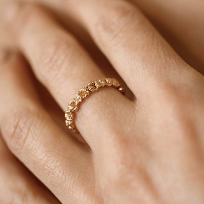 Close up of a hand with a gold floral-etched ring band with textured violet flowers and small clear gemstones.