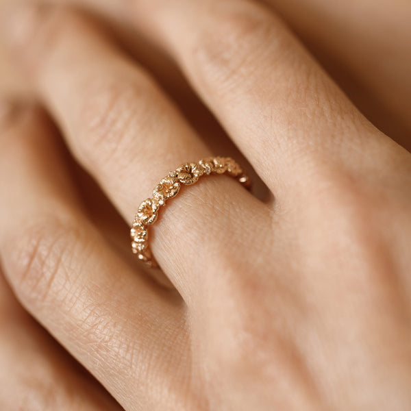 Close up of a hand with a gold floral-etched ring band with textured violet flowers and small clear gemstones.