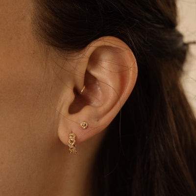 Close-up of a person wearing gold hoop earrings made up of a textured floral design and a matching stud earring.