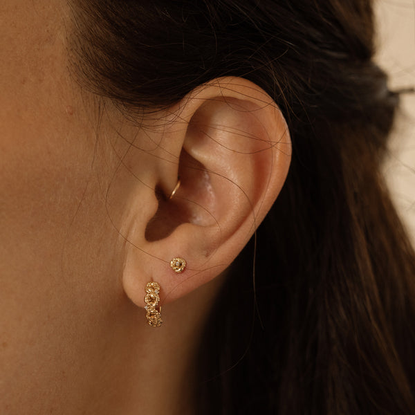 Close-up of a person wearing gold hoop earrings made up of a textured floral design and a matching stud earring.
