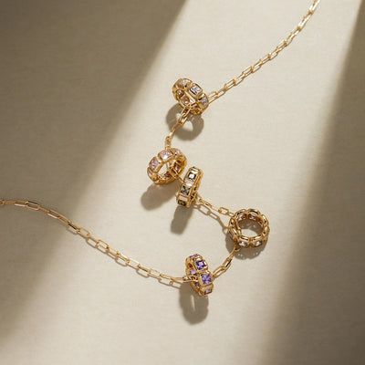A gold paperclip link necklace with round pendants, each featuring square cut bezel-set gemstones of different colors, on a light background