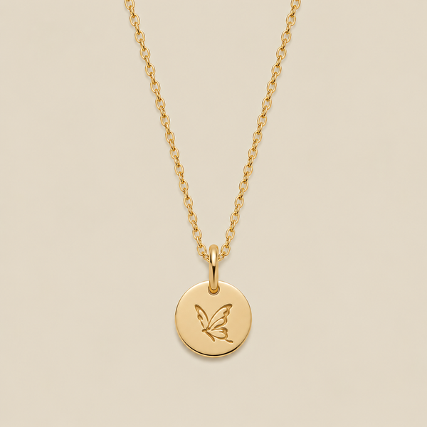 A gold chain necklace with a round gold disc pendant engraved with a butterfly, displayed against a solid beige background.